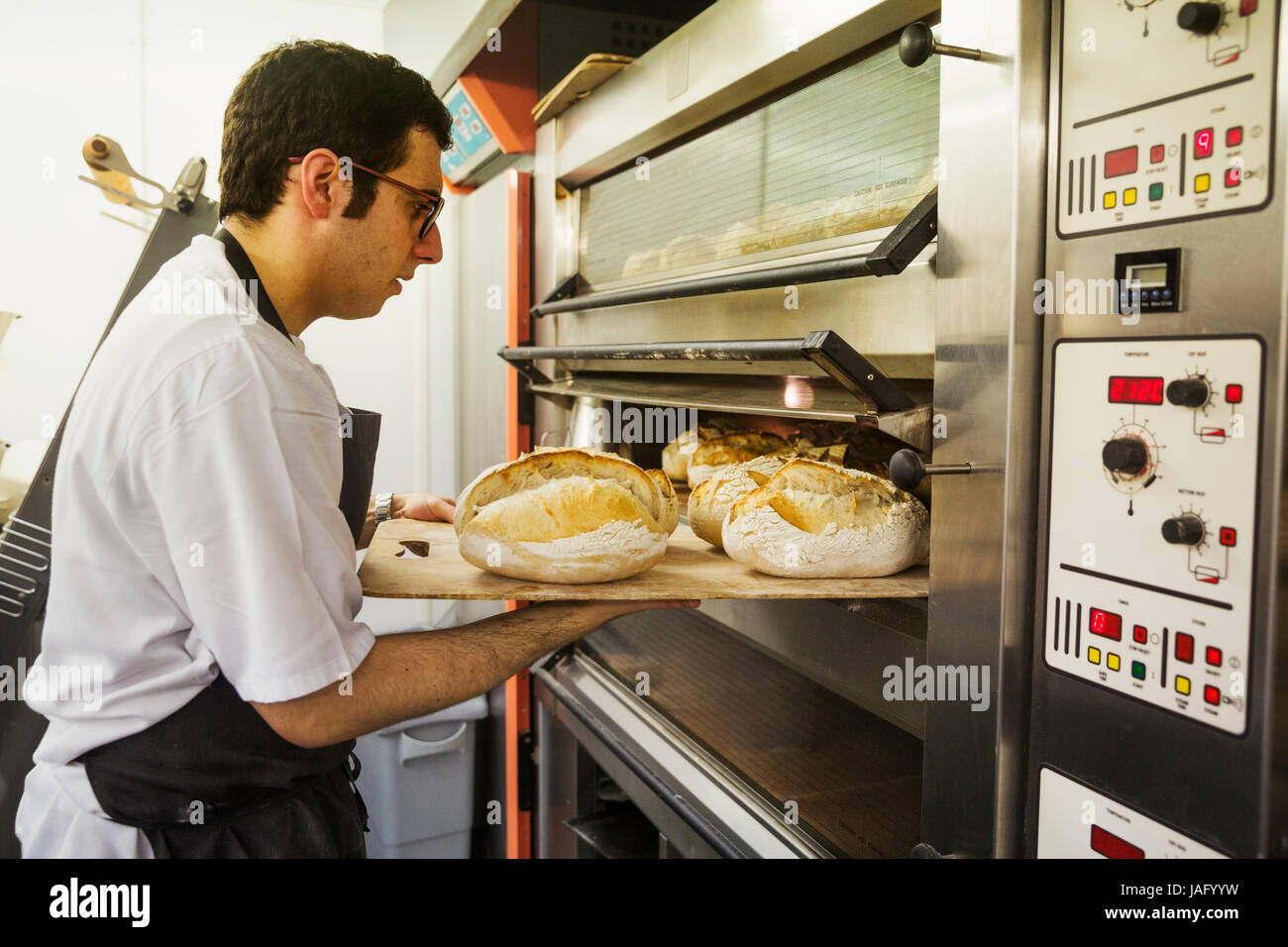 Baker removing tray with freshly baked loaves of bread from the oven Stock Photo