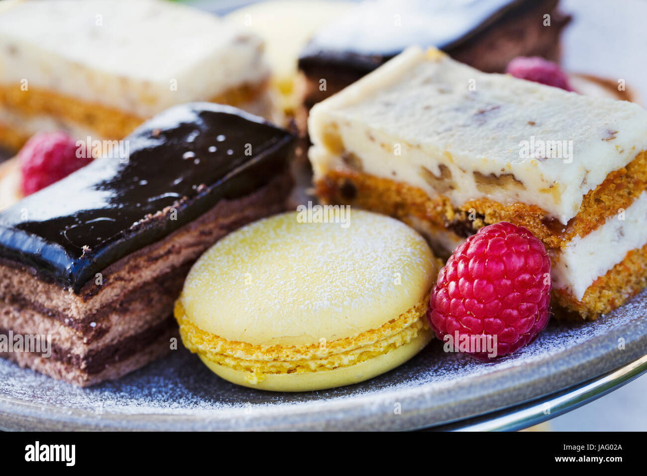 Close up of a selection of cakes, a cream slice and a macaroon and a raspberry on a plate, traditional afternoon tea. Stock Photo