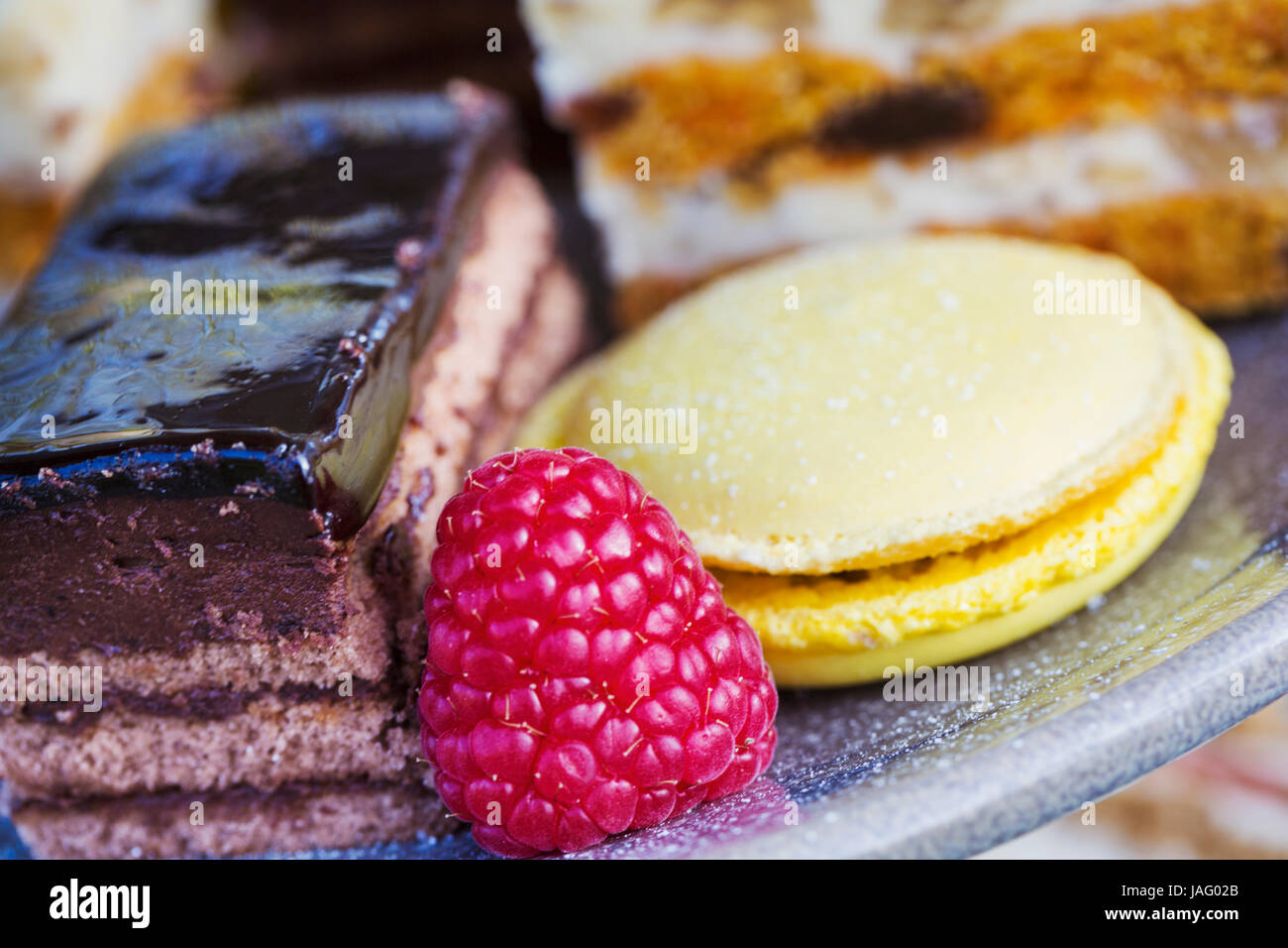 Close up of a selection of cakes, a macaroon and a raspberry on a plate, traditional afternoon tea. Stock Photo