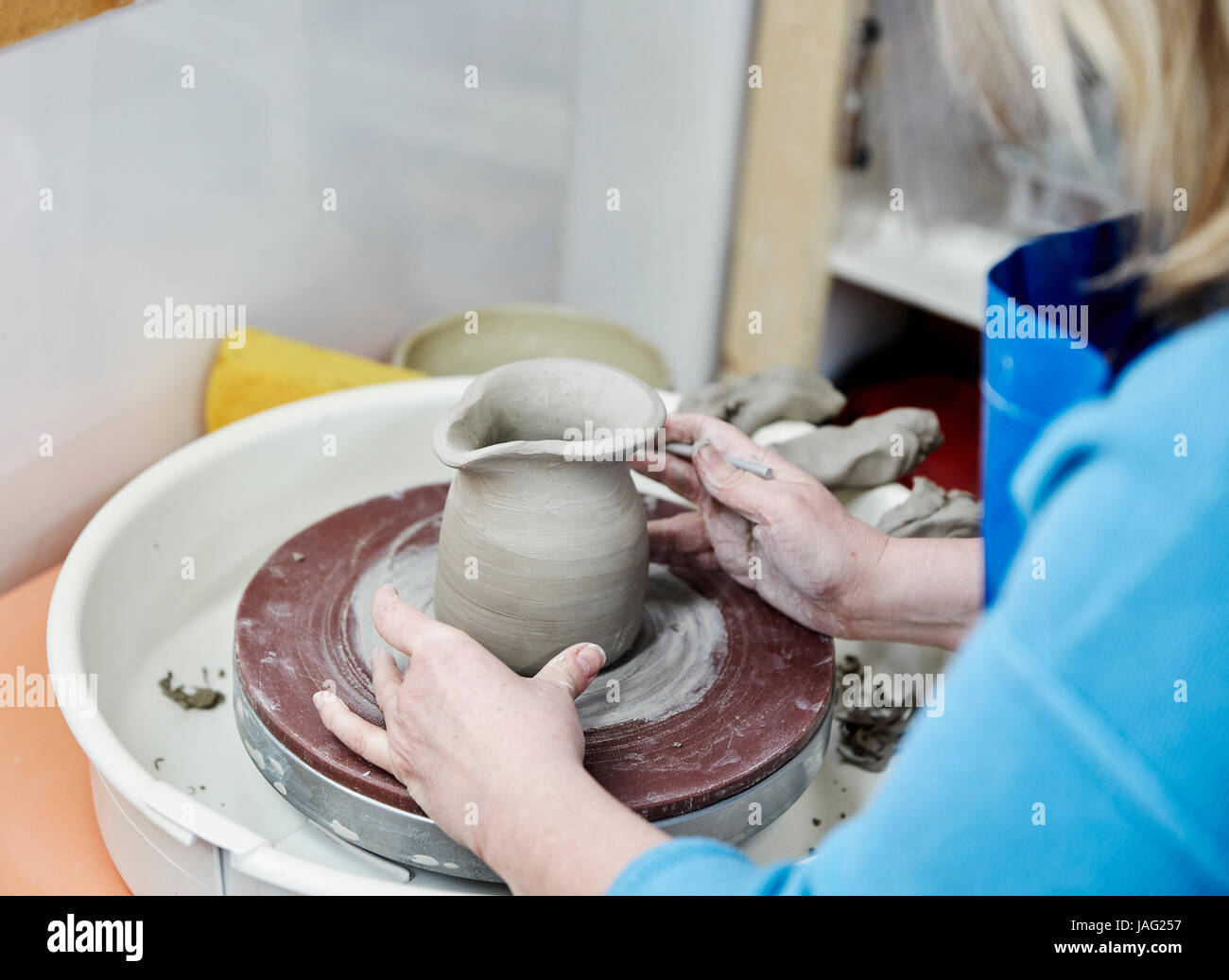 A woman using a pottery wheel, placing a small moulded thrown object, a jug with a handle in the centre of the wheel circle. Stock Photo