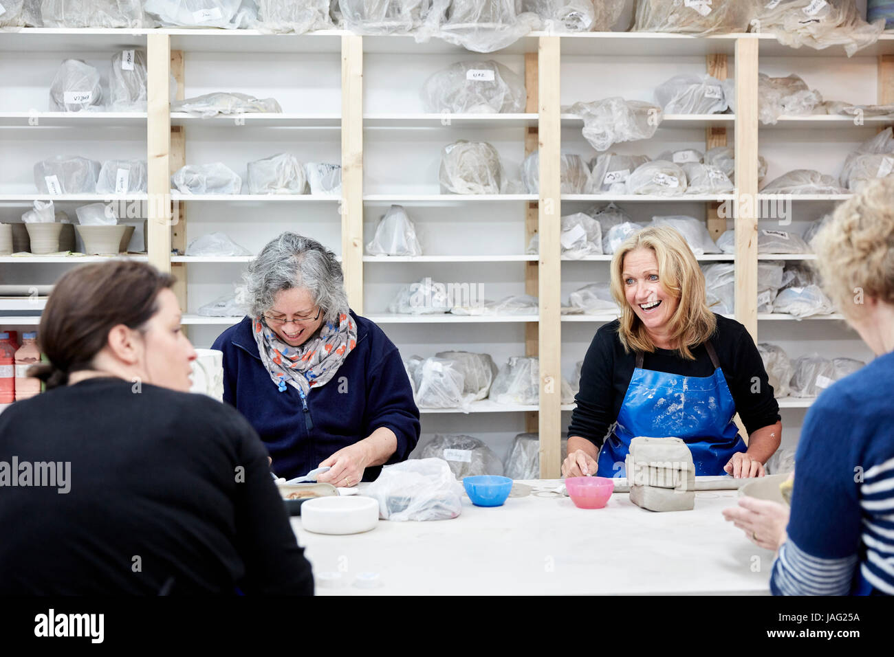 A group of four women chatting together and working on their pots in a pottery studio. Stock Photo