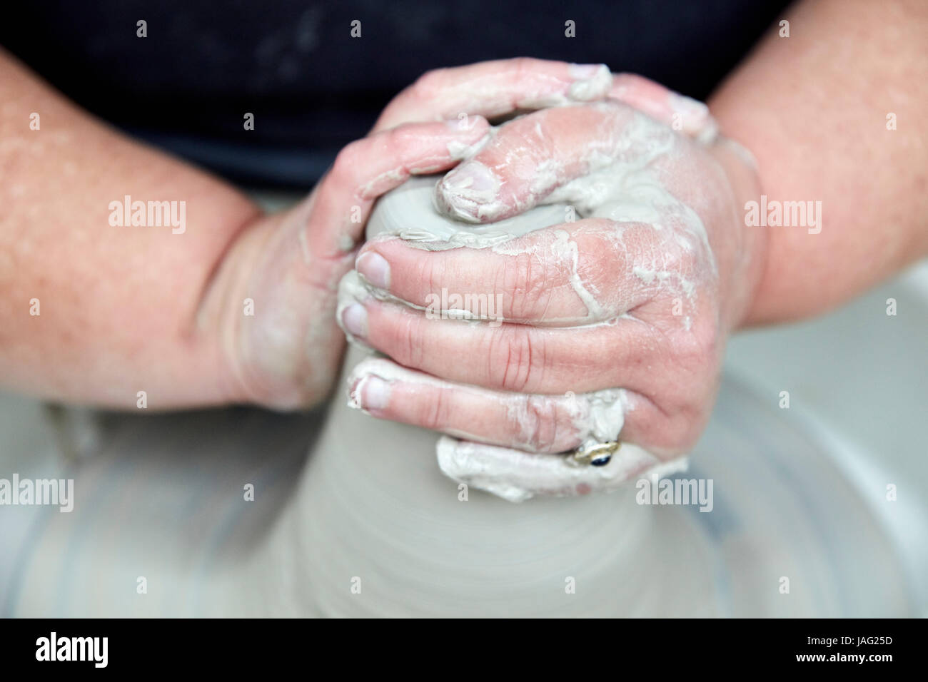 A person using a spinning pottery wheel to throw a pot using clay, hands pressing the wet clay into a basic shape for moulding on the turning wheel. Stock Photo