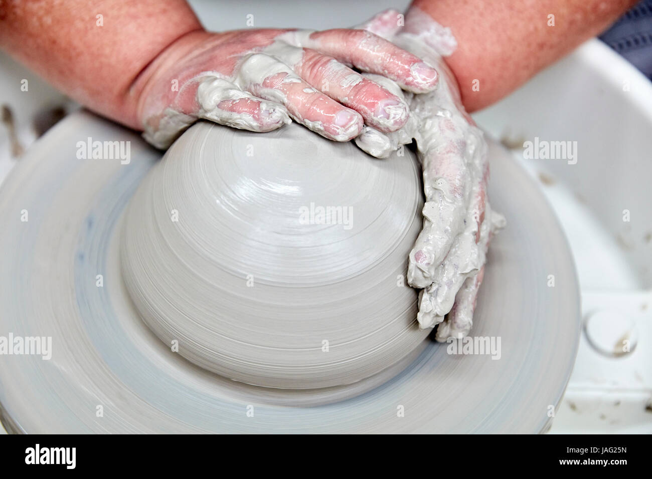 A person using a turning pottery wheel to throw a pot using clay, hands moulding the wet clay. Initial stage of throwing a pot. Stock Photo