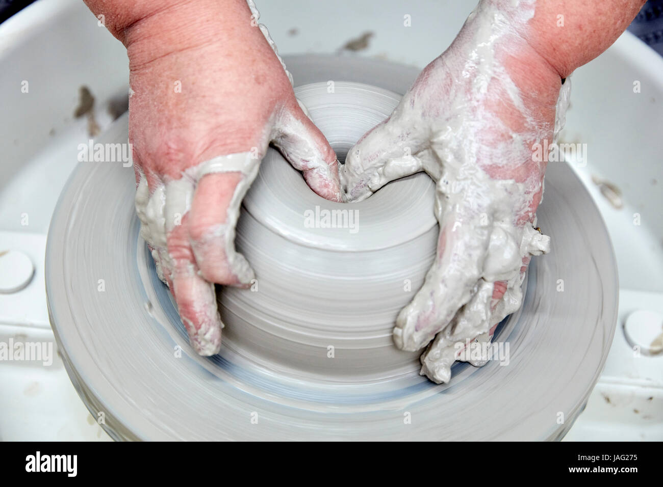 A person using a potter's wheel, throwing a clay pot and using thumbs to shape the wet clay. Seen from above. Stock Photo