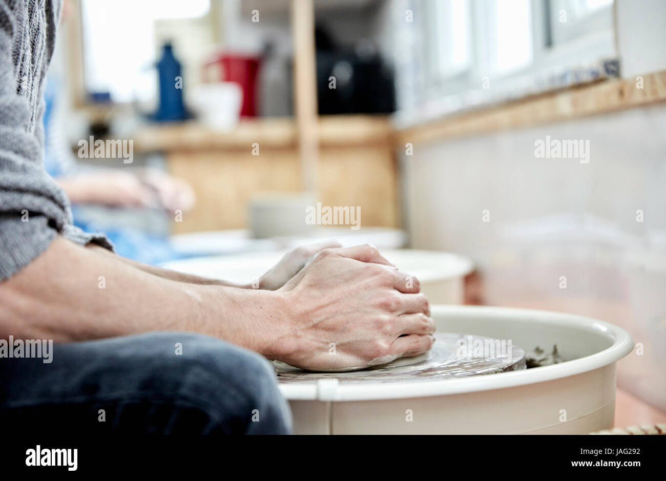 A man using a pottery wheel, with his hands on the clay, throwing pots in a pottery studio. Stock Photo