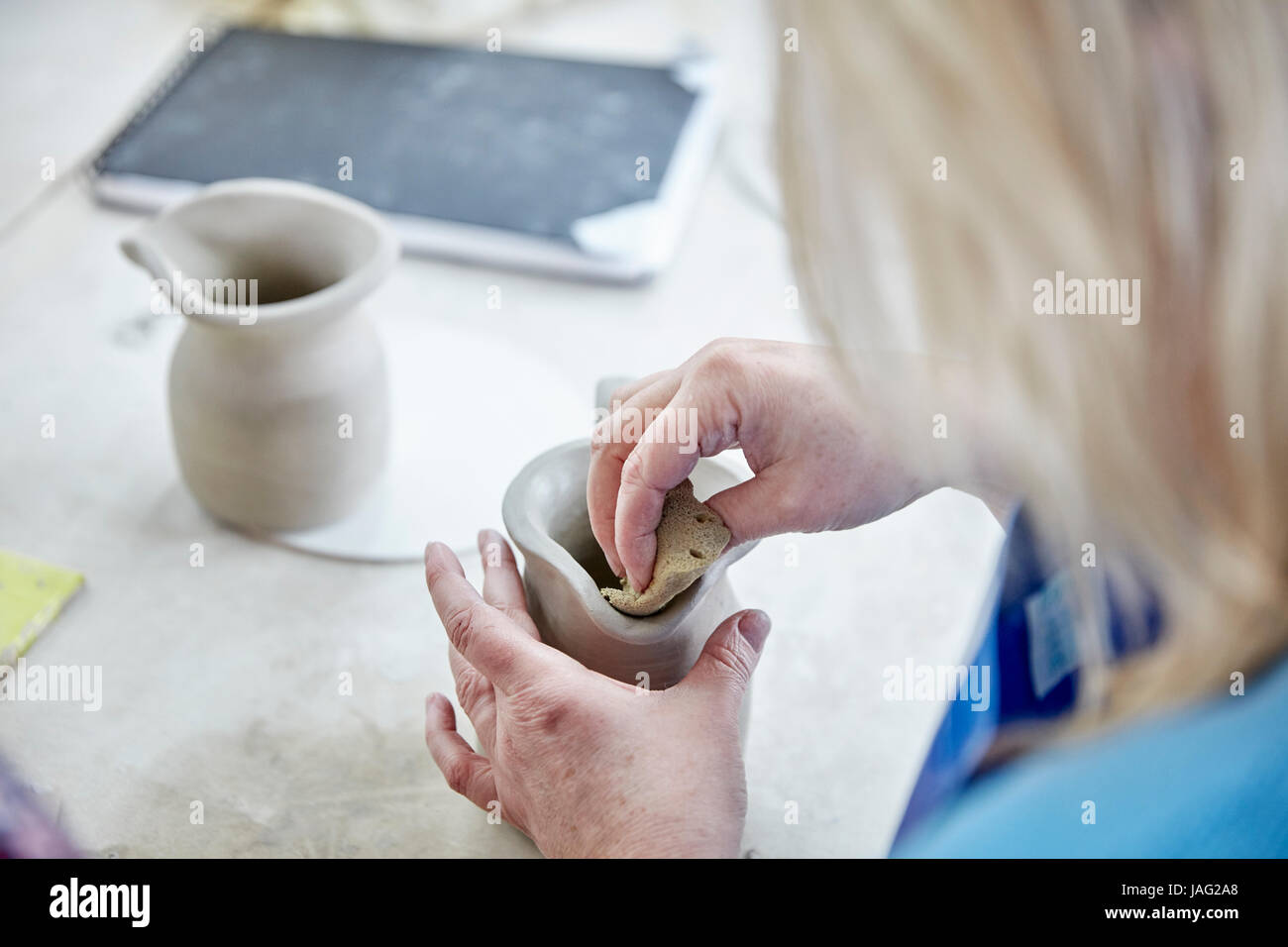 A woman using her hands to shape and smooth a wet clay jug to match another, making a pair. Stock Photo