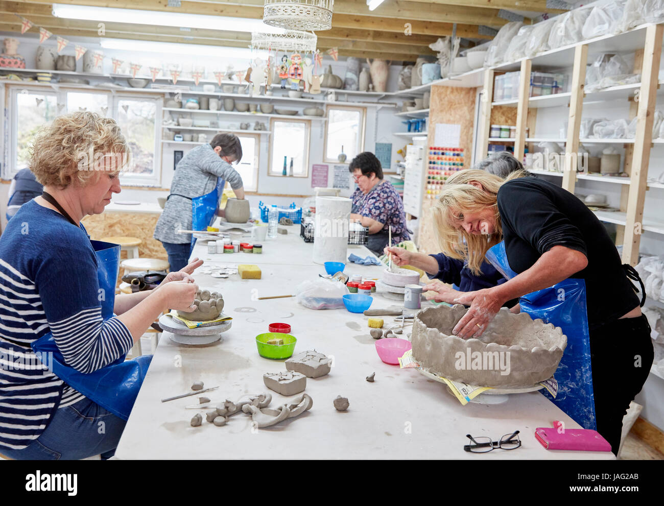 Five people, women in a pottery studio, working on handbuilding clay objects. Stock Photo