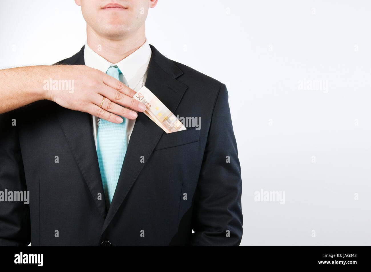 Oberkörper-Ansicht ohne Kopf eines jungen Mannes im schwarzen Anzug vor weißen Hintergrund; eine von links in das Bild hineinragende Hand steckt einen gefalteten Geldschein in die äußere Brusttasche Stock Photo