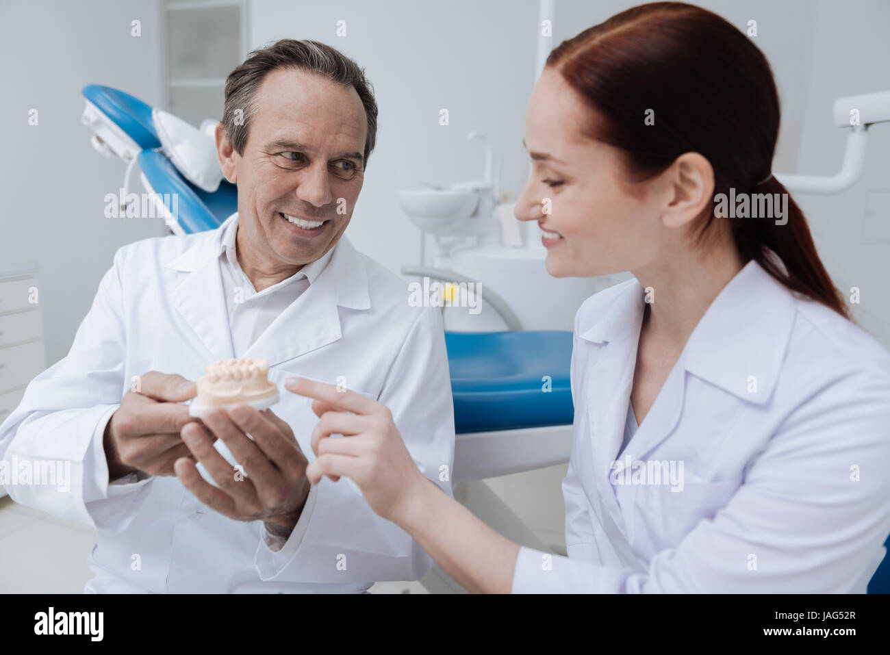 Practical lesson. Kind man showing his teeth and holding model of jaw while looking at his intern Stock Photo