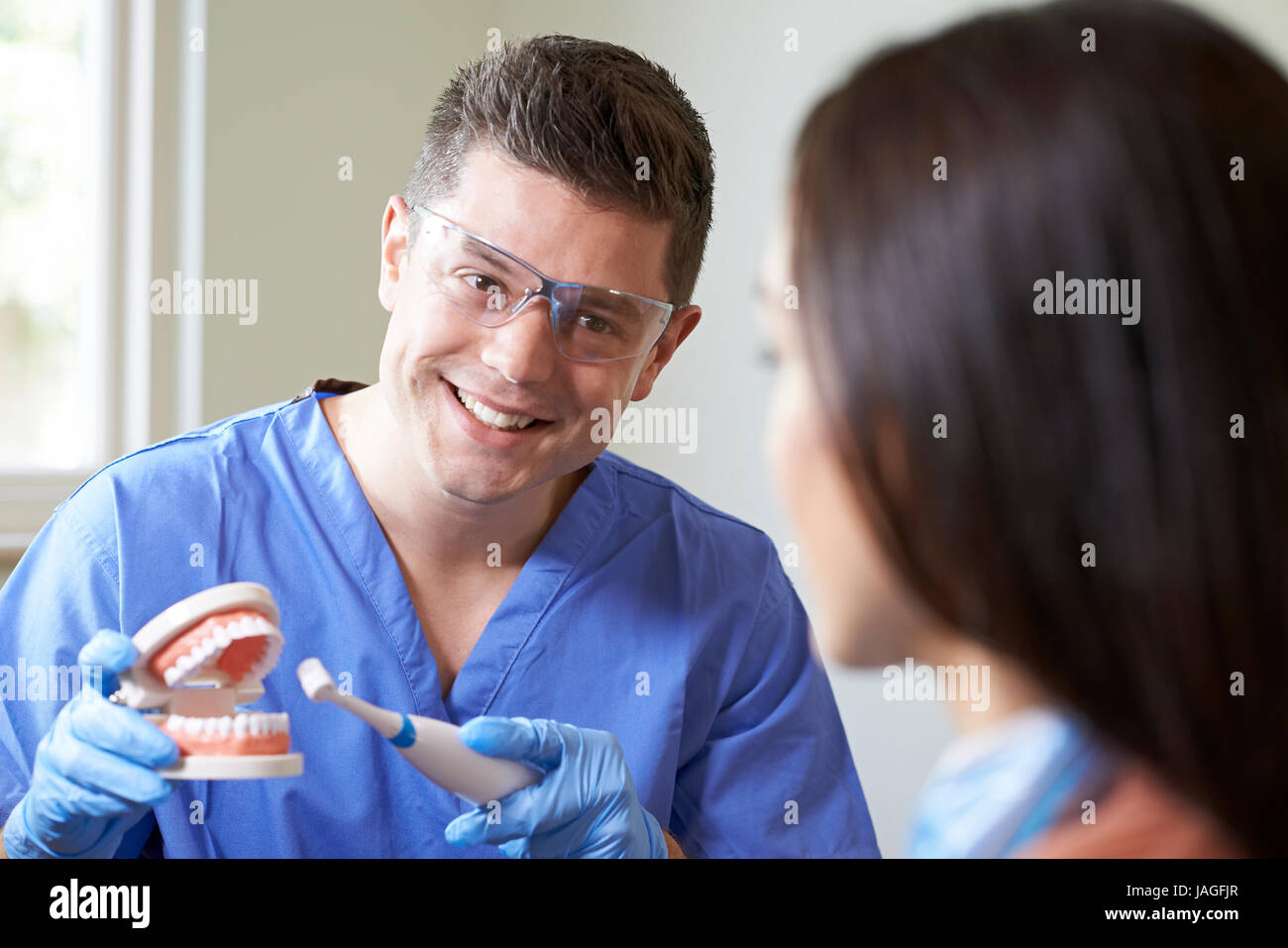 Dentist Demonstrating Use Of Electric Toothbrush To Female Client Stock Photo