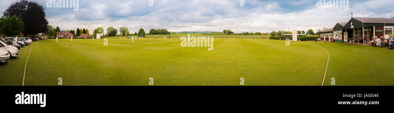 Panoramic photo showing game of Cricket being played in typical British village. Stock Photo