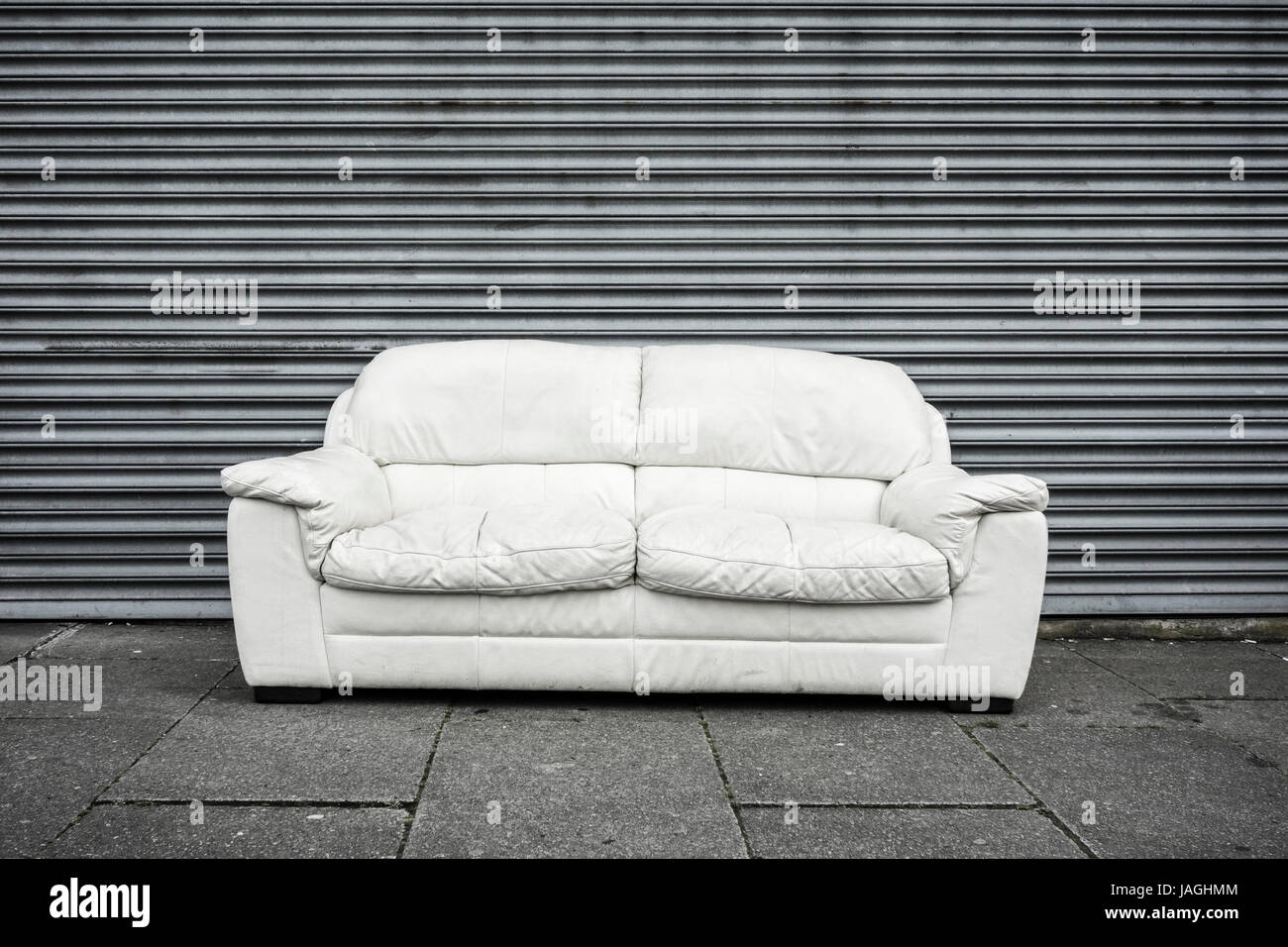 Sofa outside closed shutters in street. UK Stock Photo