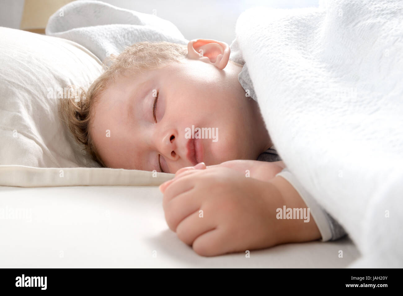 little blond boy, relaxed sleeping on her bed wrapped in a soft blanket Stock Photo