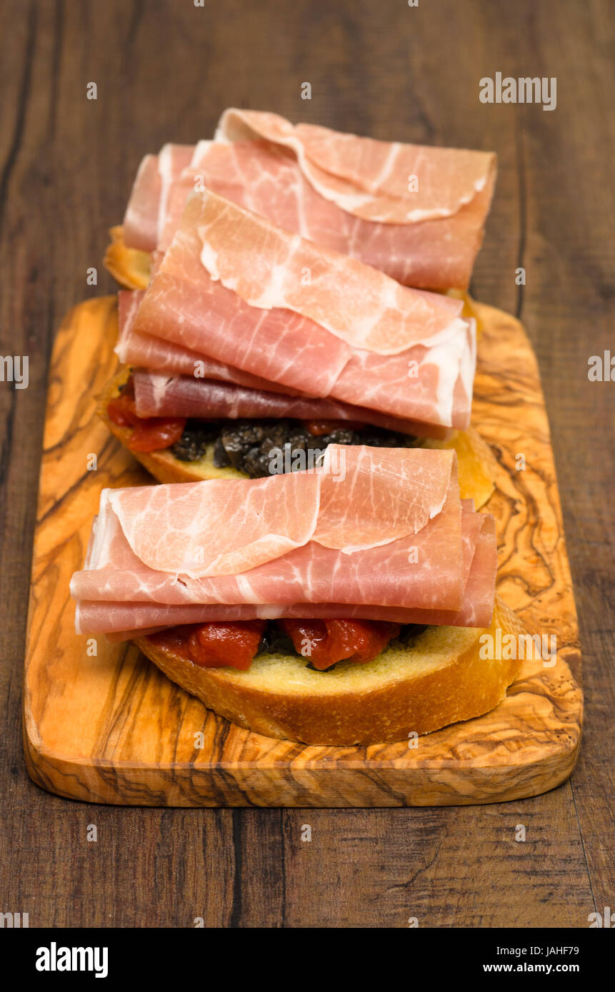 Snack aus Brot mit Olivenpaste, Tomaten und Pamaschinken im Hochformat ...