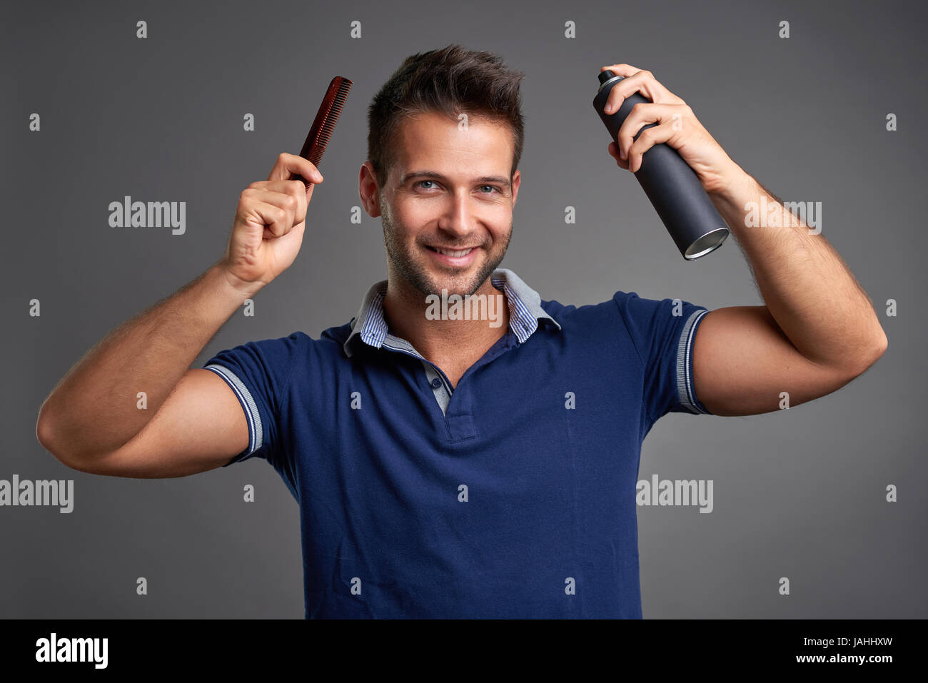 A handsome young man smiling while holding a comb and a hairspray in his hand. Stock Photo