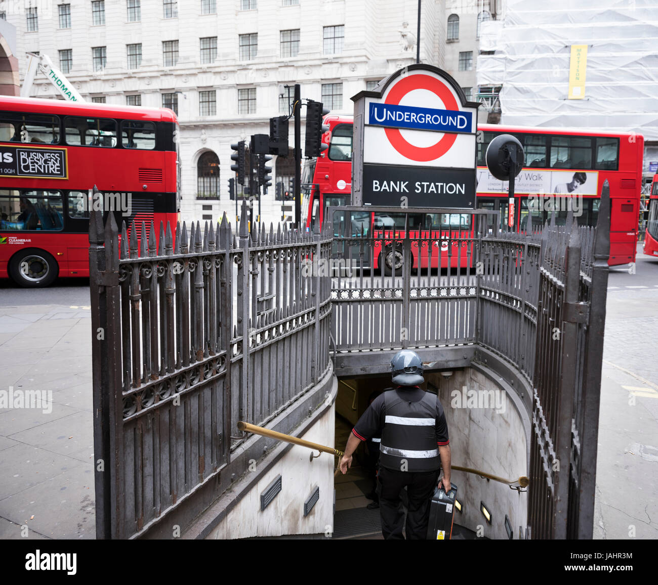 london, united kingdom, 6 may 2017: man with helmet and suitcase descends into entrance of underground station bank in london while busses pass by Stock Photo