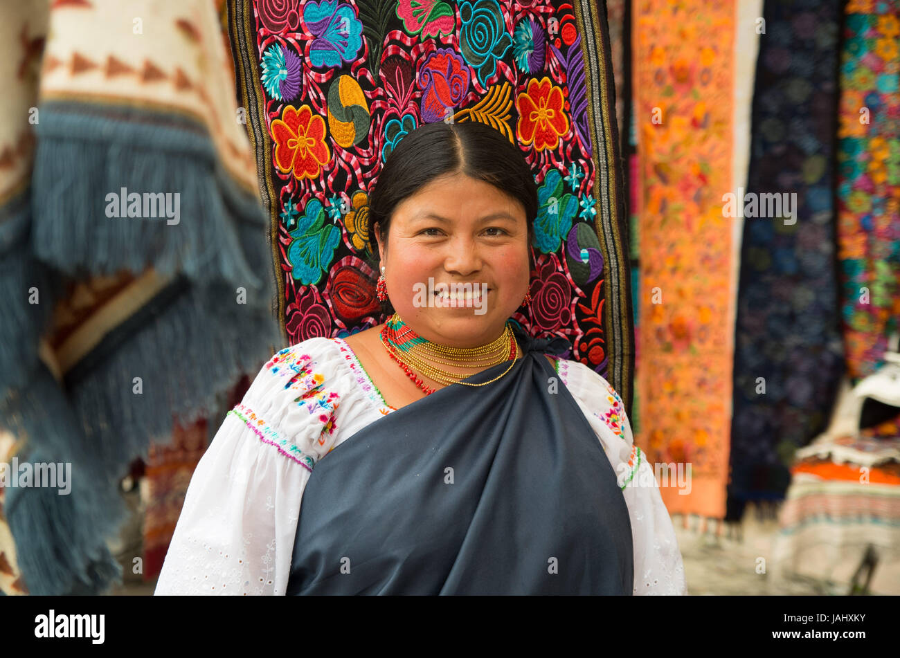 OTAVALO, ECUADOR - MAY 17, 2017: Close up of an unidentified hispanic indigenous woman wearing andean traditional clothing and necklace, posing for camera in colorful fabrics background Stock Photo