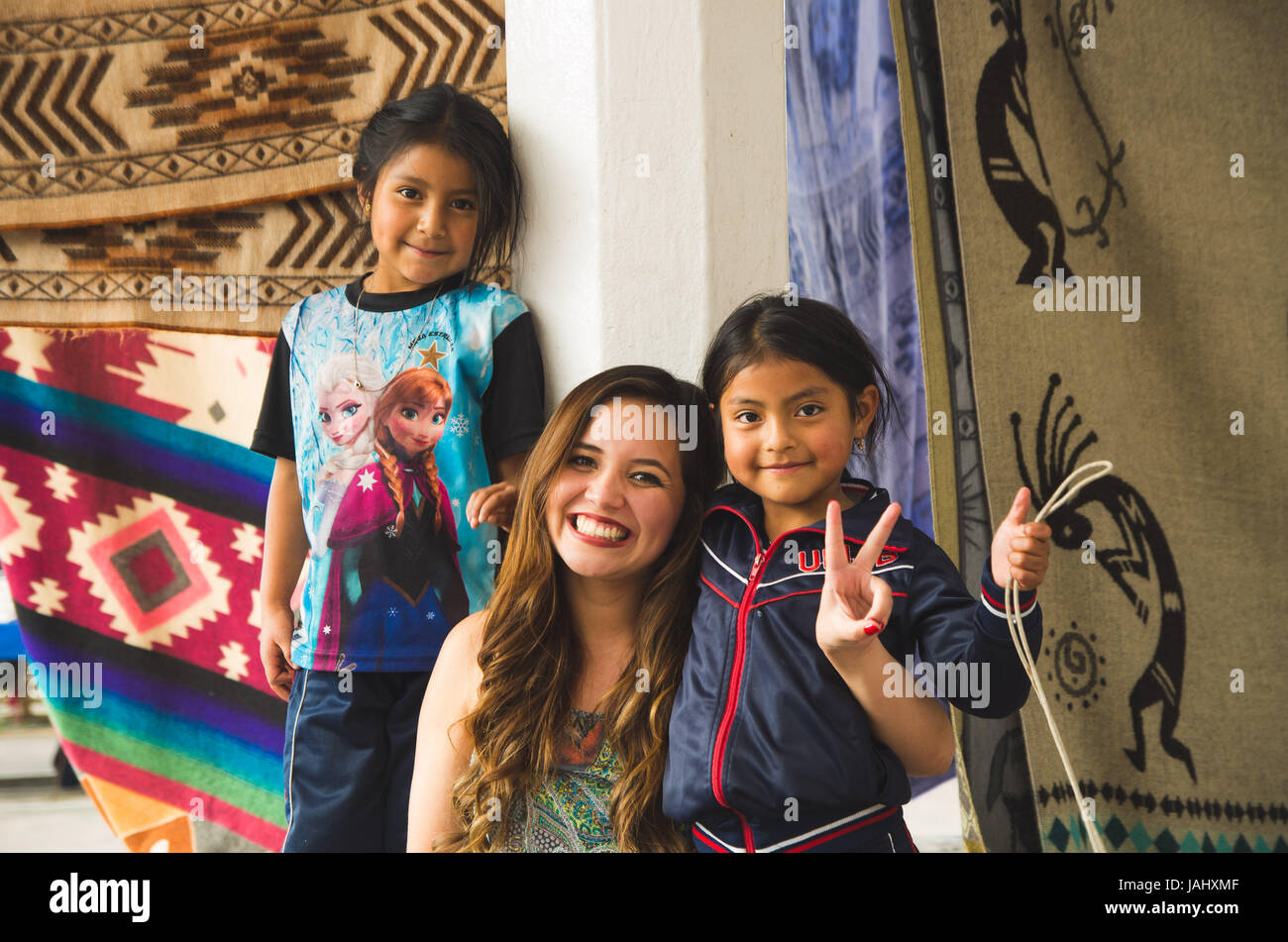 OTAVALO, ECUADOR - MAY 17, 2017: Beautiful young woman hugging to two beautiful little indigenous girls, in colorful fabrics background Stock Photo