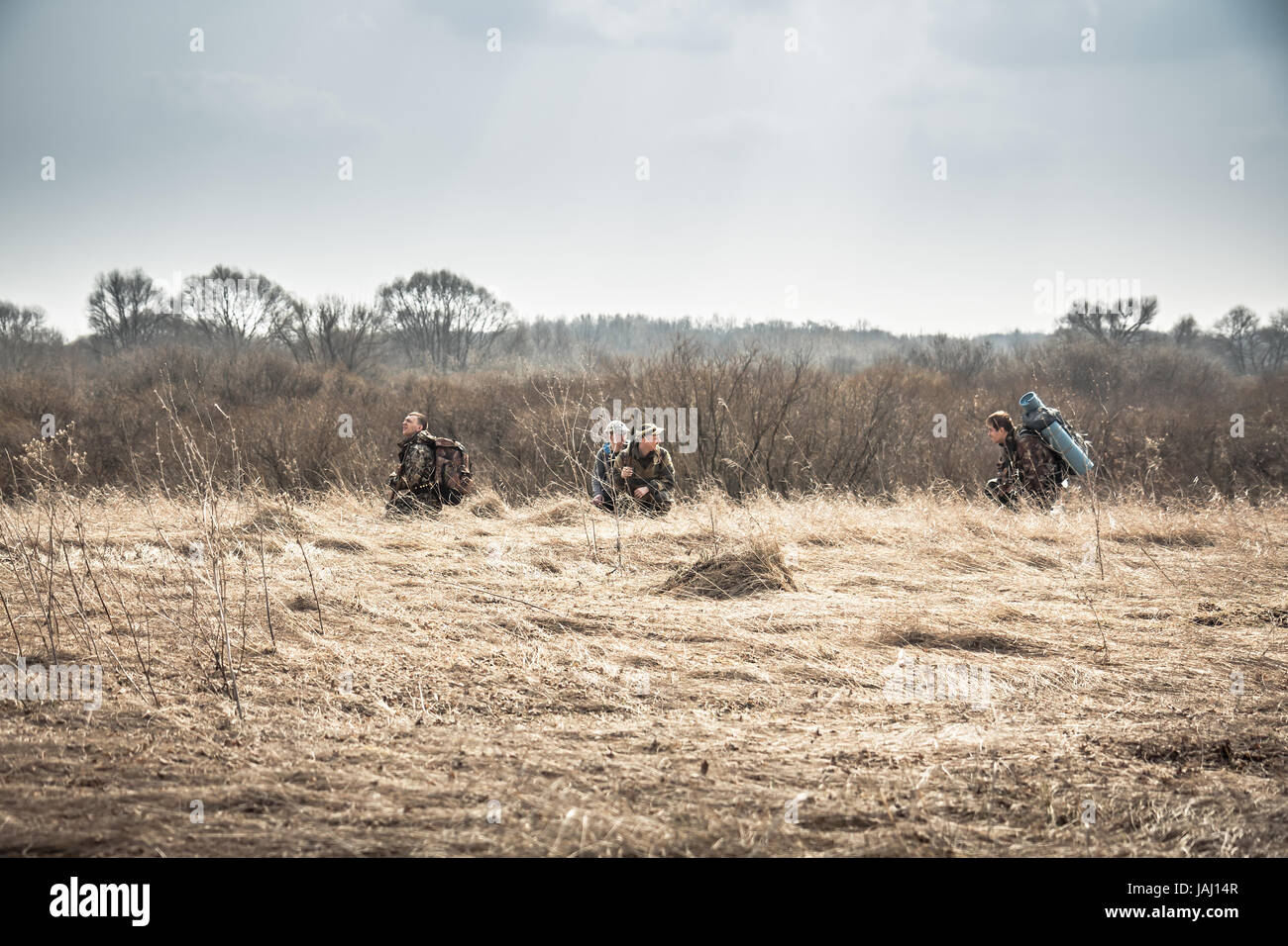 Group of hunters hiding in rural field with dry grass during hunting season in overcast day Stock Photo