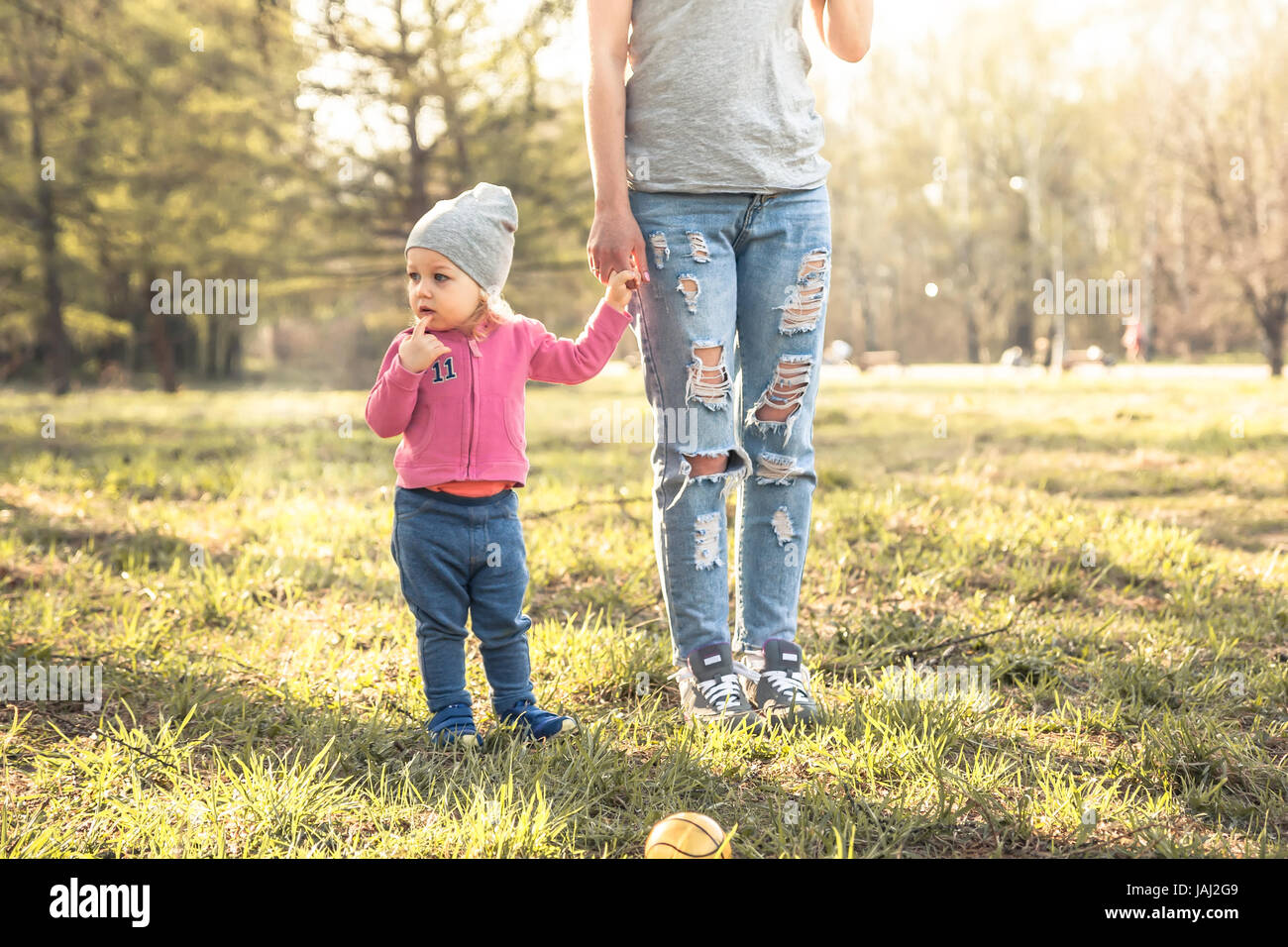 Child with mother standing together with holding hands in summer park on grass. Main subject is child. Unrecognizable mother on photo.  Concept for to Stock Photo