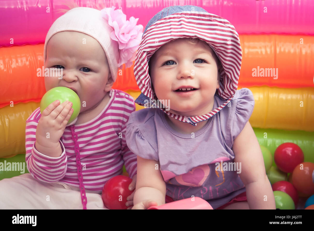 Two smiling cheerful cute baby girls playing together in entertainment park with toys symbolizing children friendship and happy childhood Stock Photo