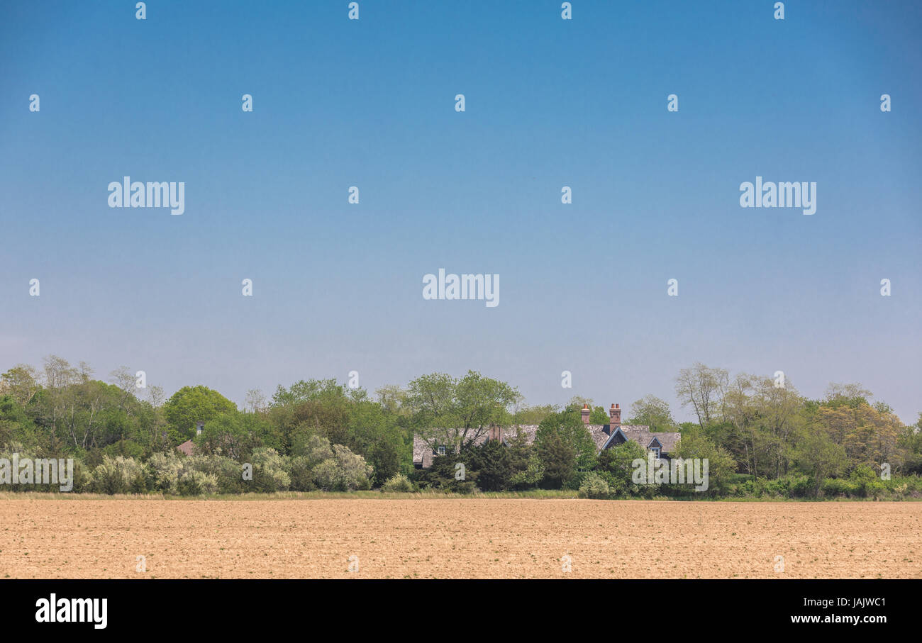 a freshly plowed field bordered by a stand of tree with a house nearby Stock Photo