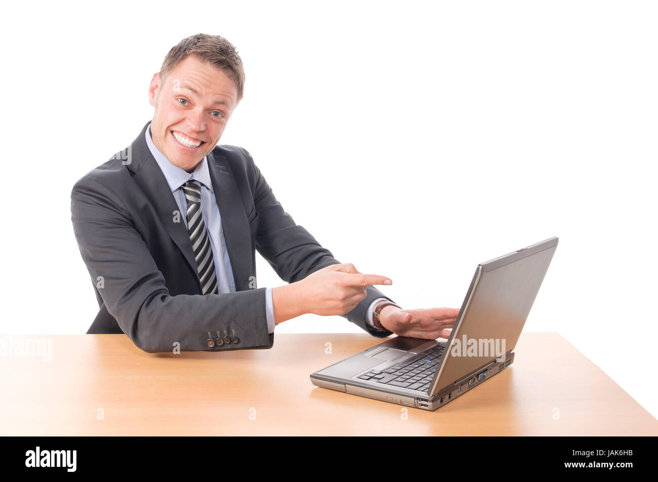 Junger Geschäftsmann in Anzug und Krawatte sitzt am Schreibtisch und arbeitet begeistet an seinem Notebook-PC. Freigestellt vor weißem Hintergrund Stock Photo