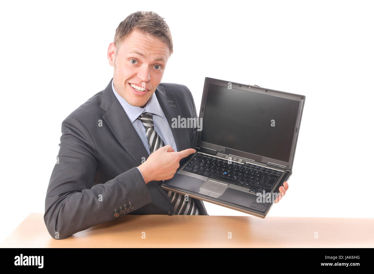 Junger Geschäftsmann in Anzug und Krawatte sitzt am Schreibtisch und zeigt stolz auf seinen Notebook Bildschirm. Freigestellt vor weißem Hintergrund Stock Photo