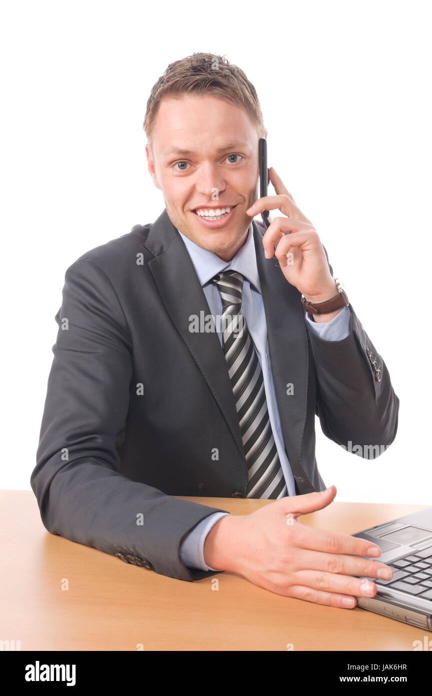 Junger Geschäftsmann in Anzug und Krawatte sitzt am Schreibtisch und arbeitet an seinem Notebook-PC. Dabei telefoniert er mit einem Kunden und schließt ein geschäft ab. Freigestellt vor weißem Hintergrund Stock Photo