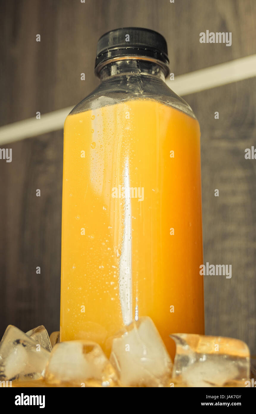 Bottle of orange juice with some ice around. Transparent plastic bottle