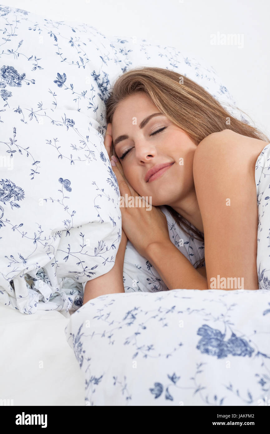Junge brünette hübsche Frau schäft auf einem Kissen in blauer Bettwäsche Stock Photo