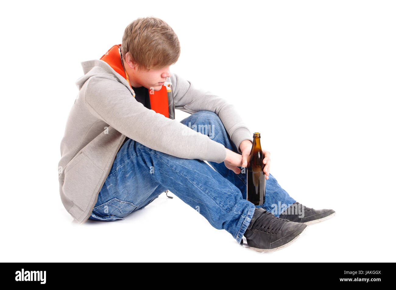 Junger Mann mit kurzen blonden Haaren sitzt auf dem Boden mit Bierflaschen und ist betrunken, isoliert vor weißem Hintergrund Stock Photo