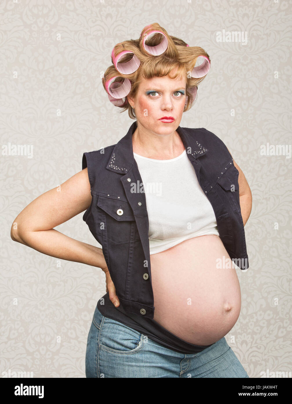 Serious pregnant female in curlers with hands on hips Stock Photo