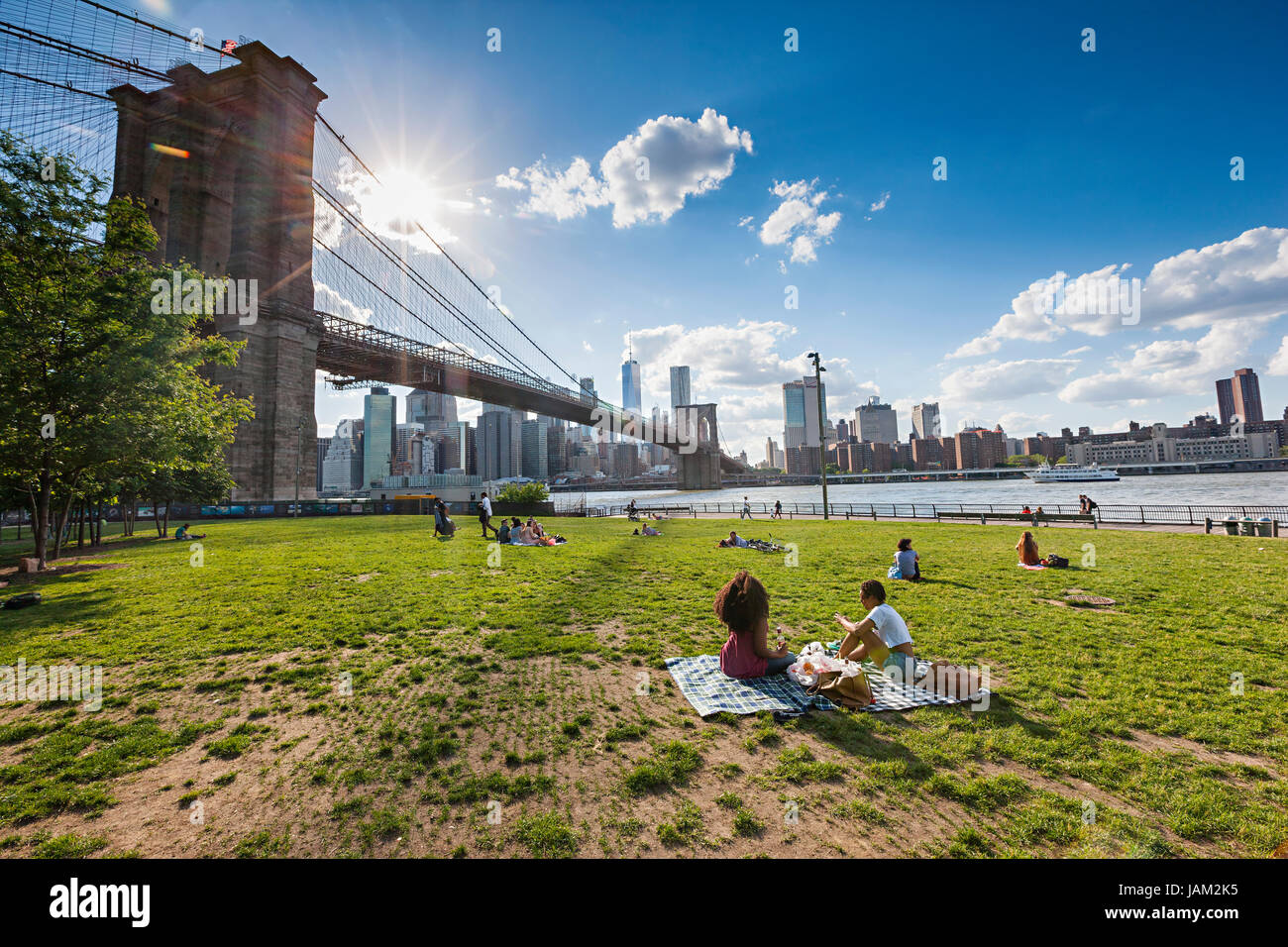 People enjoying free time on sunny day near Brooklyn Bridge in New York City Stock Photo