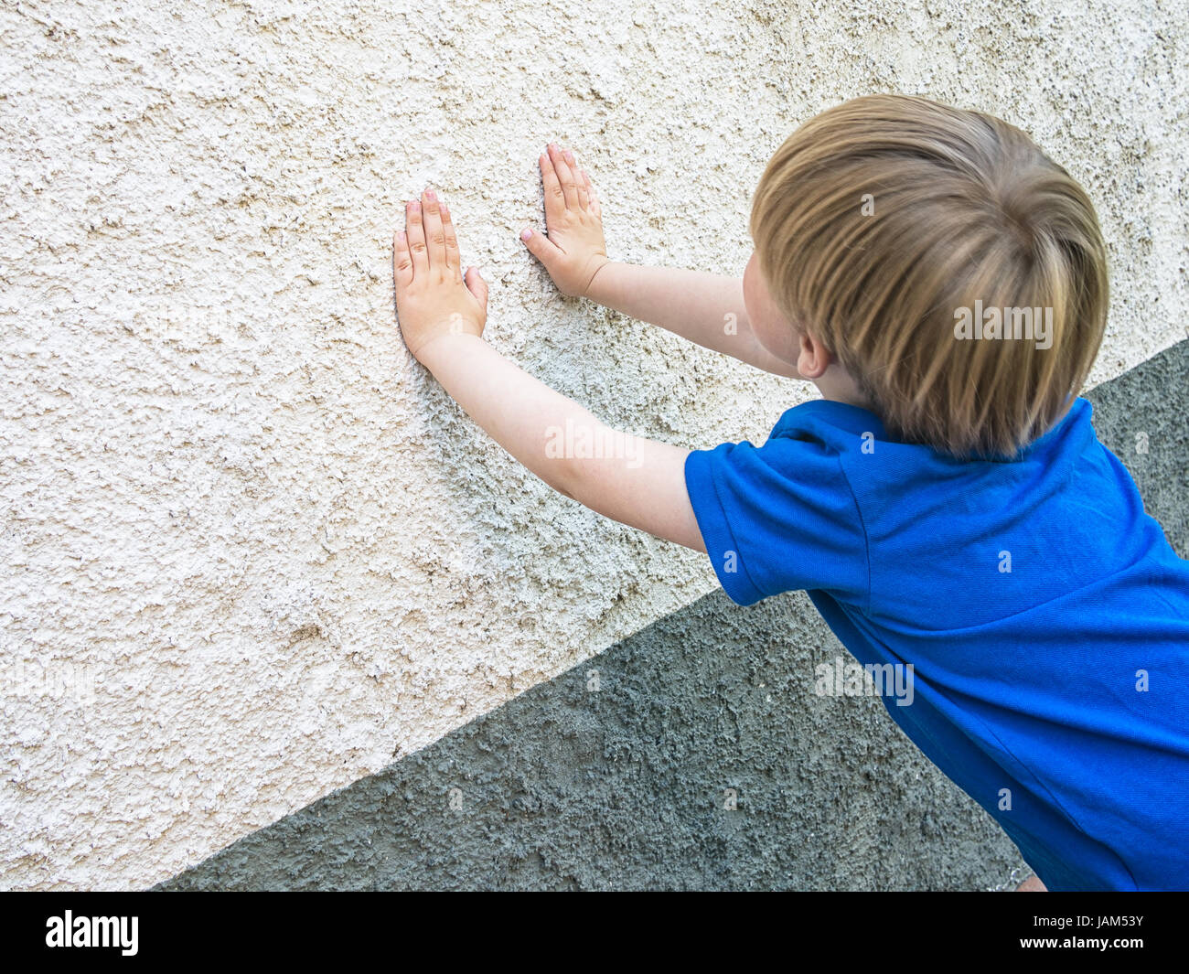 Hide and seek game. Cute blond child. Note focus on hands and wall for greater anonymity of boy. Stock Photo