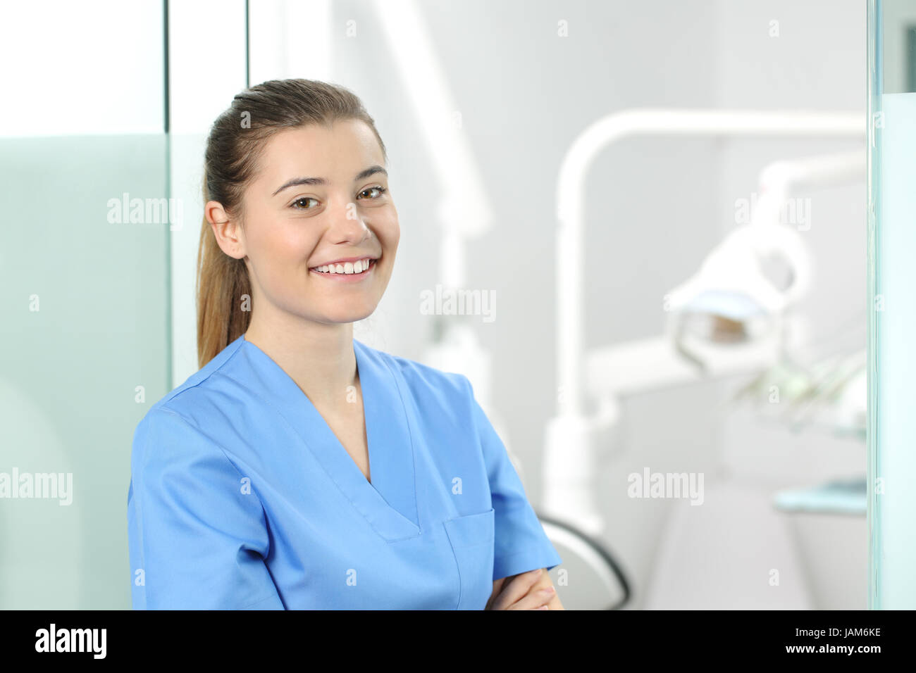 Portrait of a young female doctor wearing a blue coat posing in a dentist office with medical equipment in the background Stock Photo