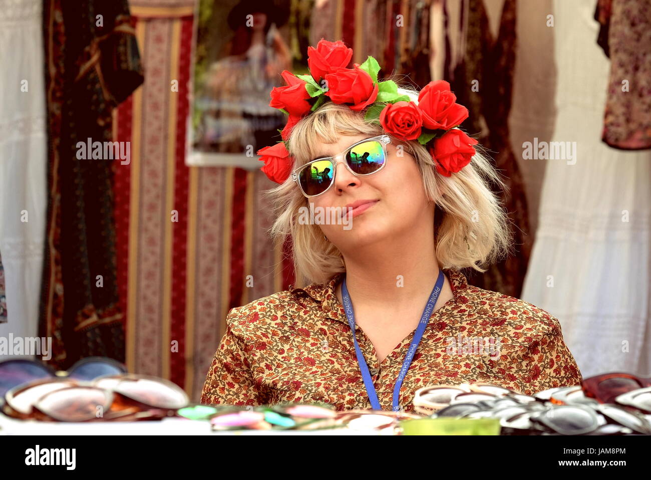 Woman with red roses in hair wearing  1950s dress selling retro clothing,  vintage items, antiques at outdoor festival market stall, Stock Photo