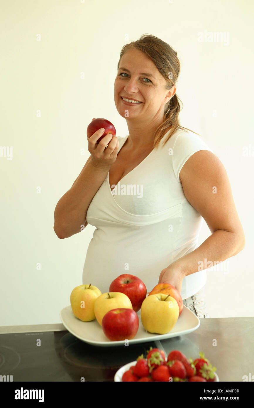 Woman,pregnant,apple,eat,happily,portrait,person,young,smile,joy,prejoy,cuisine,plate,fruit,apples,strawberries,fruit,fruits,healthy,yellow,red,vitamins,T-shirt,white,V-neck,gestation,due date,firstborn,single parents, Stock Photo