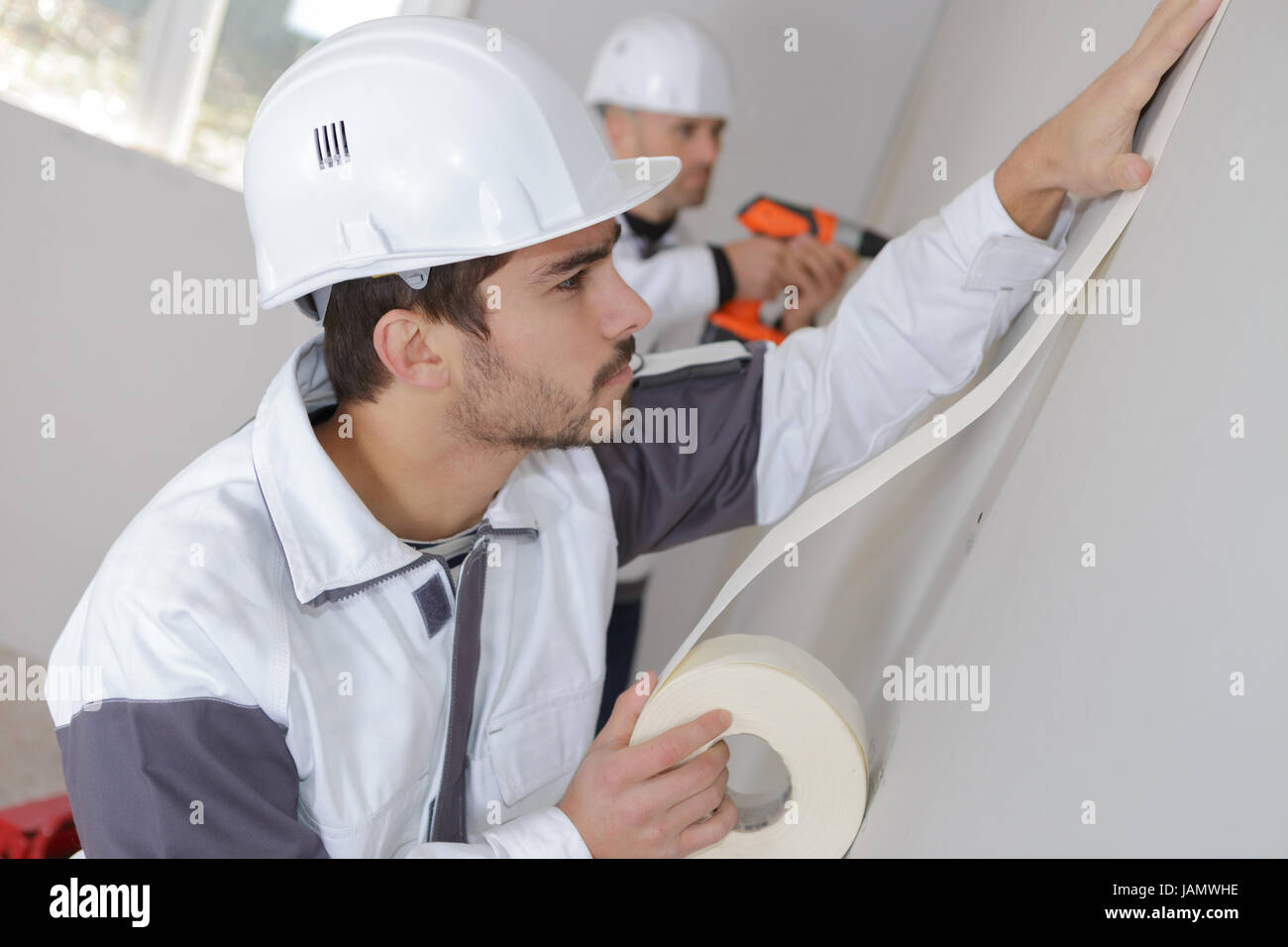 worker protecting batten moulding with masking tape before painting