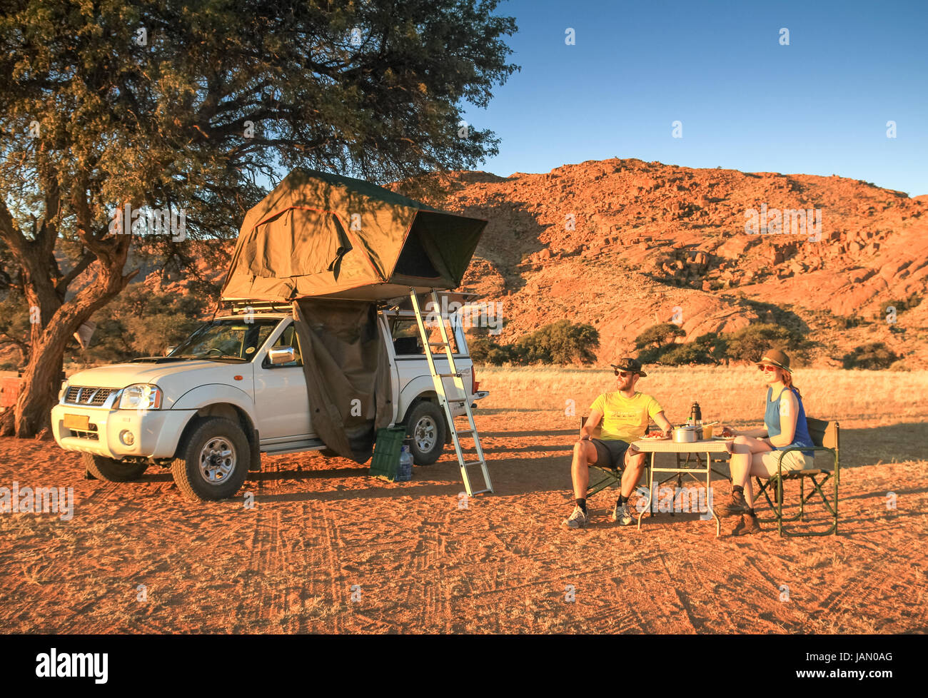 Couple camping in desert having dinner. Orange sunset sunrise light. Stock Photo