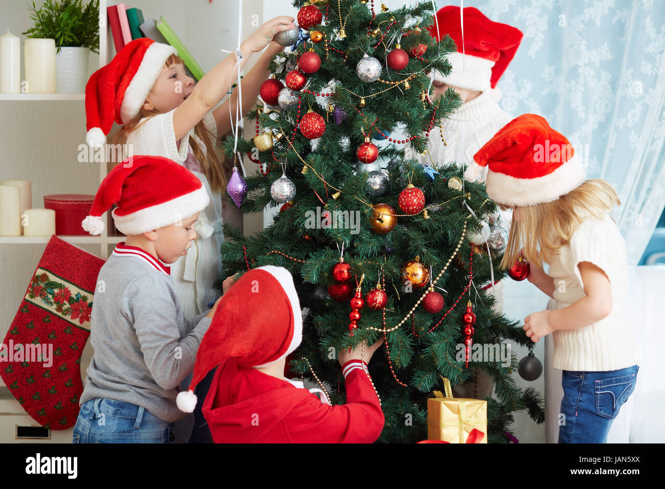 Group Of Adorable Kids In Santa Caps Decorating Xmas Tree Stock