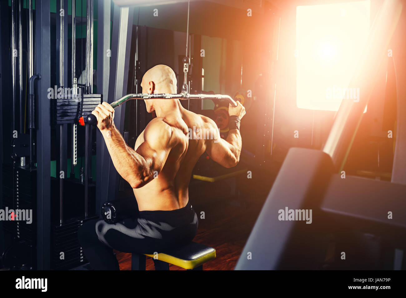 very power athletic guy bodybuilder, execute exercise with gym apparatus, on broadest muscle of back Stock Photo