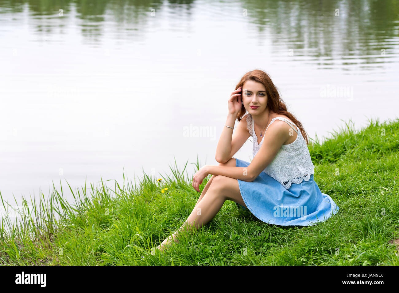 A girl with long hair sits on the grassy shore of the lake Stock Photo ...