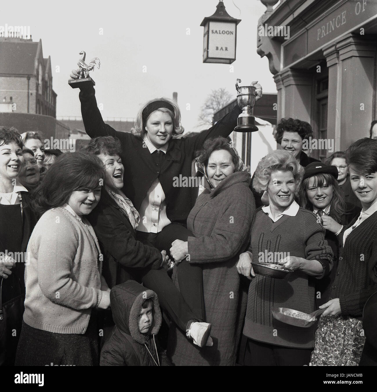 1965, historical, picture shows the winning lady holding aloft her trophies outside the Prince of Wales pub in the annual pancake race on the Old Kent Road, London, SE1. Stock Photo