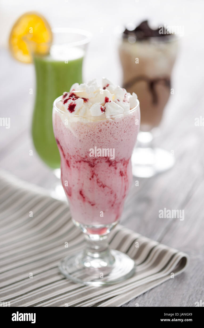 Sweet red berries cocktail with whipped cream and crashed meringue served in long glass. Fresh desserts composition with chocolate shake and kiwifruit mousse on the background. Stock Photo