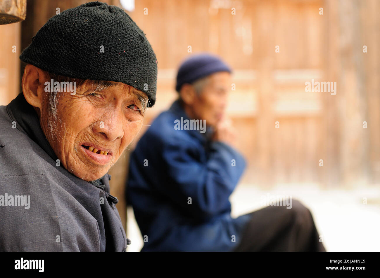 ZHAOXING, CHINA - 11 NOVEMBER 2010:  Old Chinese resting on the doorstep of his cottage in the village Zhaoxing Stock Photo
