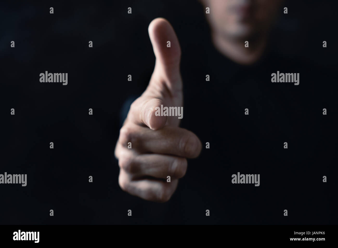 closeup of a young caucasian man pointing his forefinger to the front pretending that it is a gun, against a black background Stock Photo