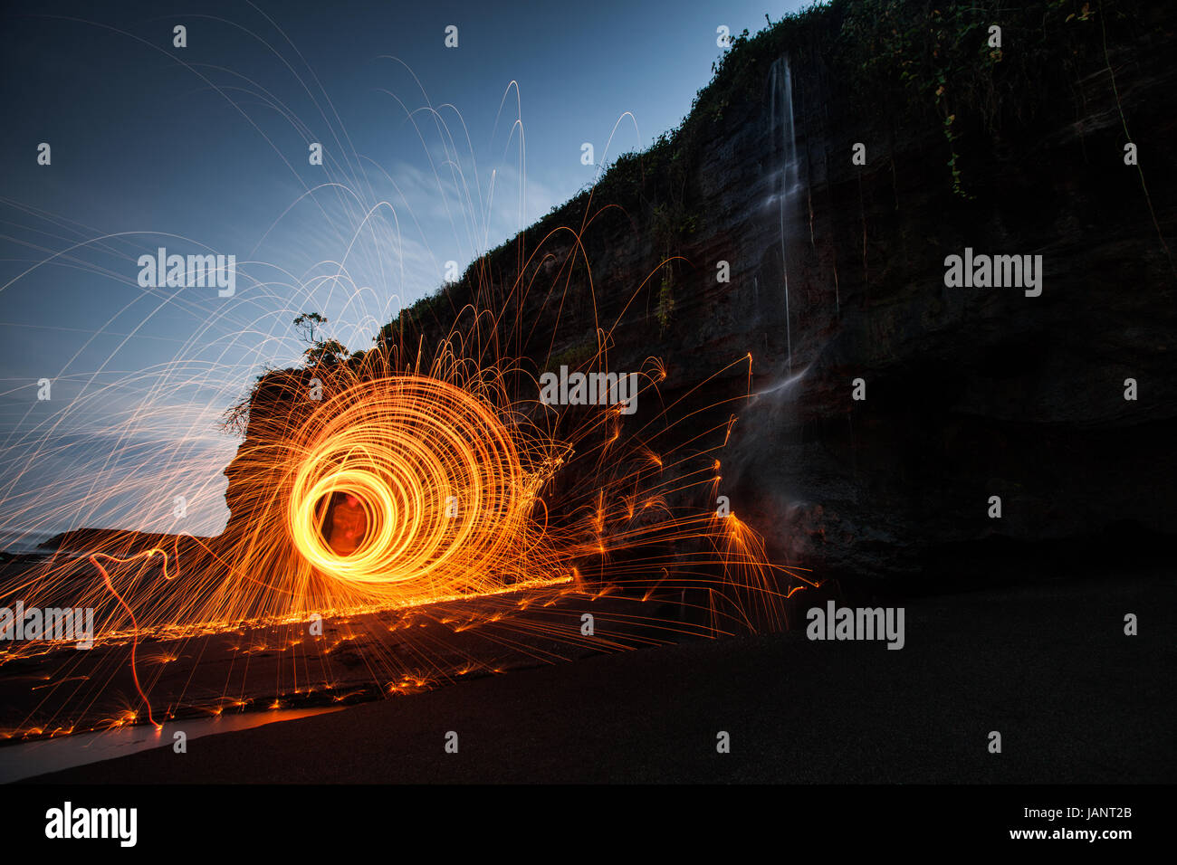 Circles of light created by light painting with burning wire wool at a beautiful spot on a Bali beach with a waterfall tumbling down a cliff face Stock Photo