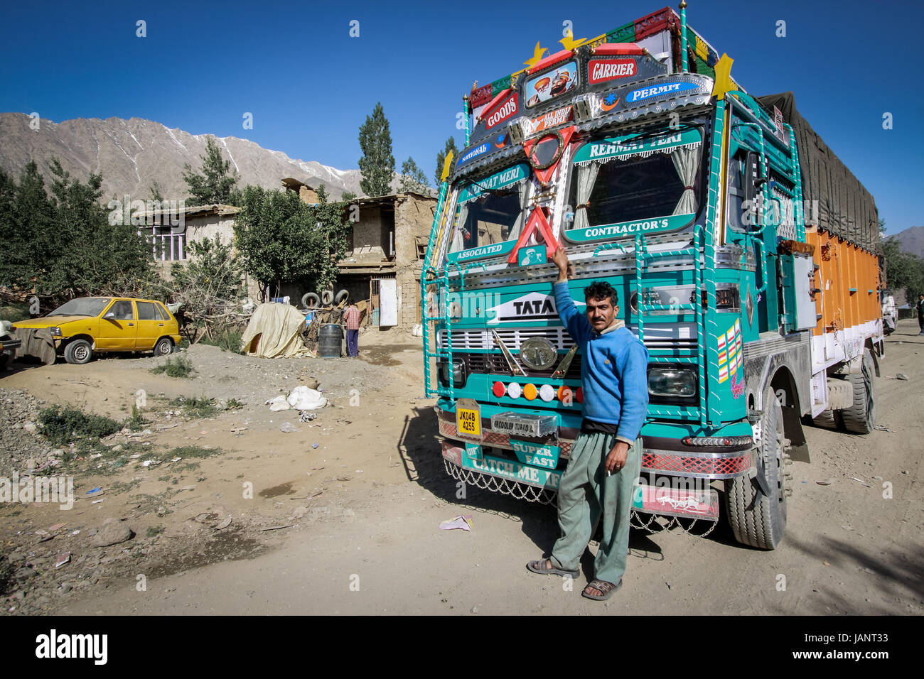 Indian truck driver standing beside his well loved and colorful Indian truck in the extreme terrain of the Indian Himalaya. Highest roads in the world Stock Photo
