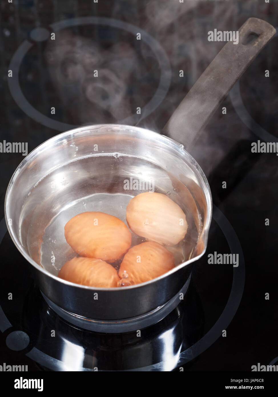 simmering chicken eggs in metal pot on electric stove in kitchen Stock